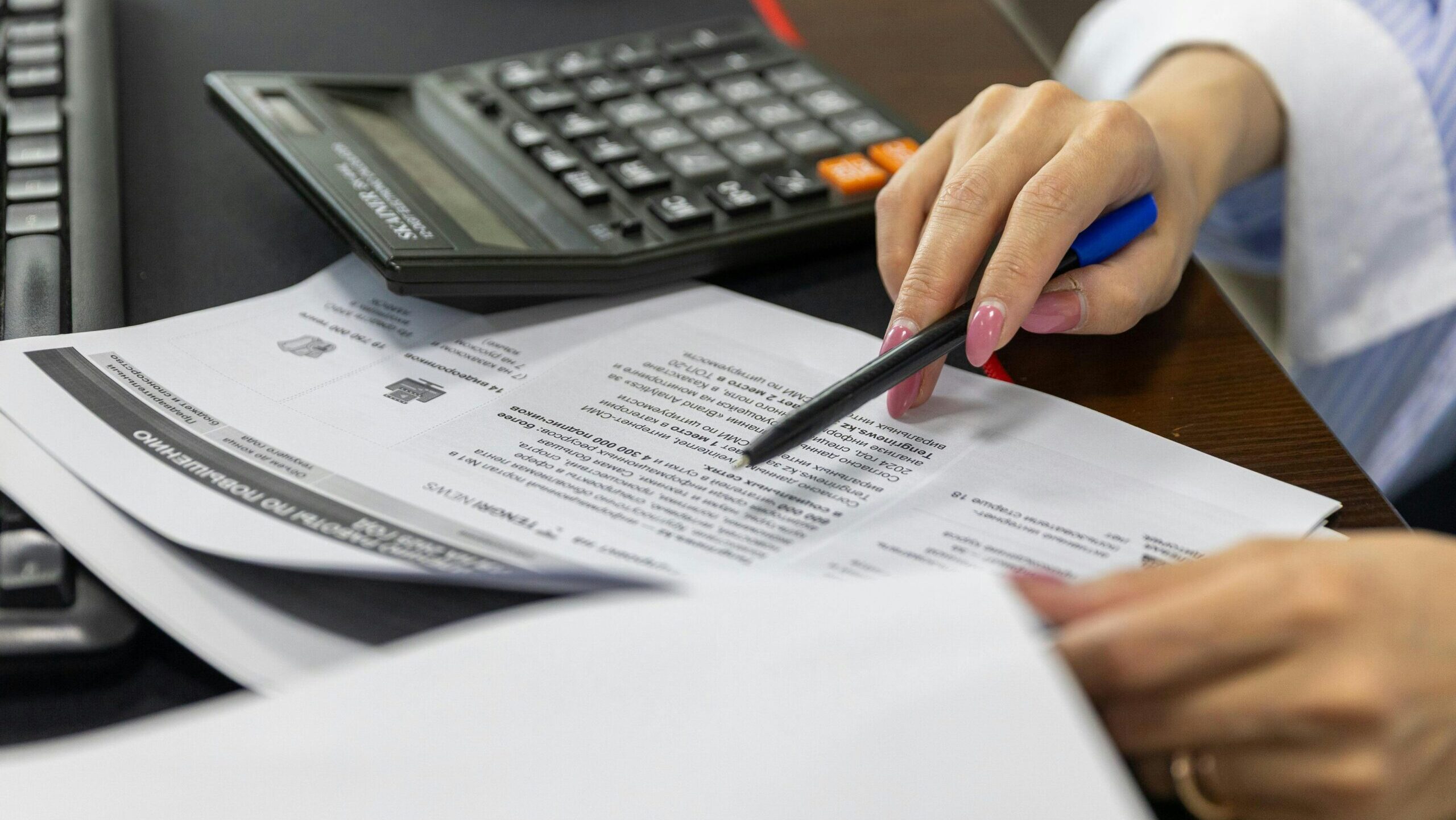 pexels-photo-33175657-33175657 Close-up of a woman's hand reviewing financial documents with a calculator.